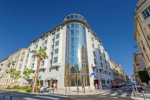 A modern hotel with a curved glass facade, multiple balconies, and a pedestrian walkway. - Goldstar Appartements Nice (Nice)