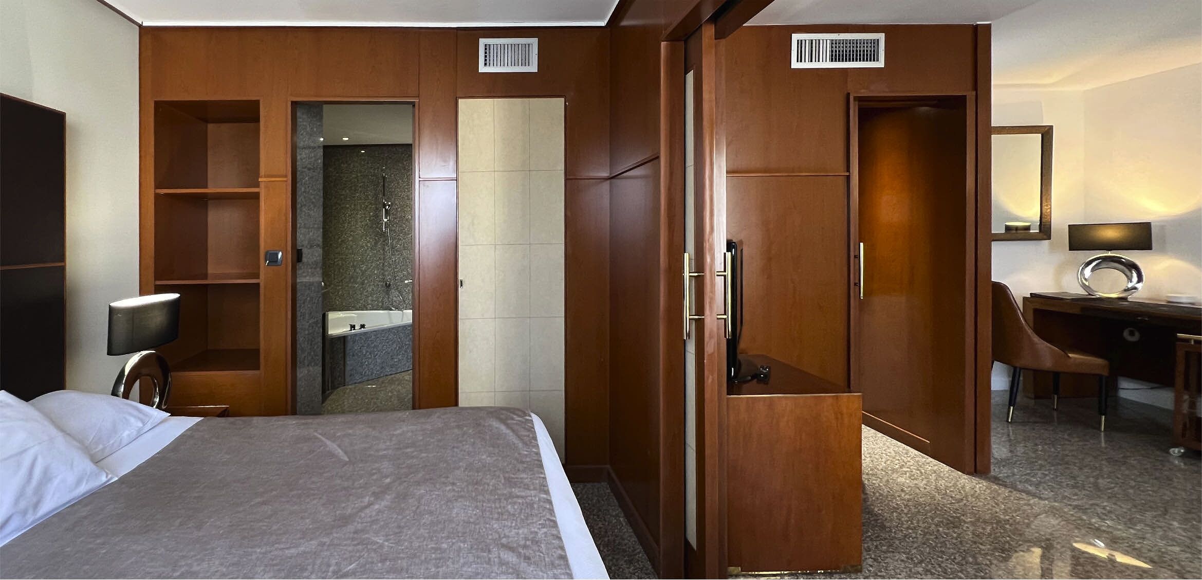 Una habitación de hotel con cama, escritorio, silla, espejo y armario.