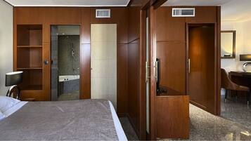 Una habitación de hotel con cama, escritorio, silla, espejo y armario.