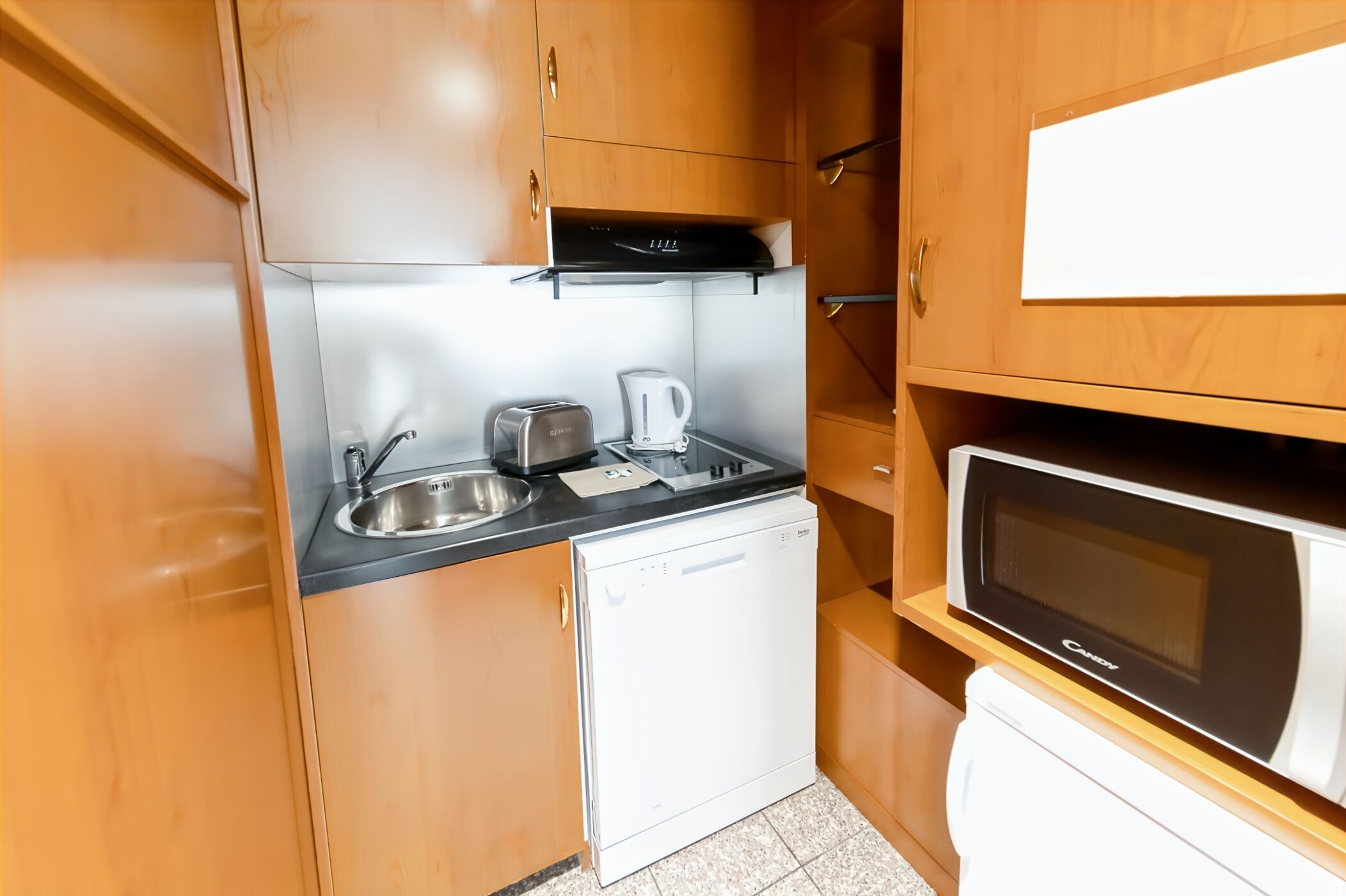 A compact kitchenette with a sink, toaster, kettle, and microwave.