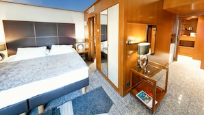 Una habitación de hotel moderna con una cama grande, una mesita de noche con lámpara, un espejo y una pequeña zona de estar con una revista.