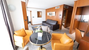 Una habitación de hotel moderna con sofá, dos sillones, una mesa redonda y una pequeña planta en maceta.