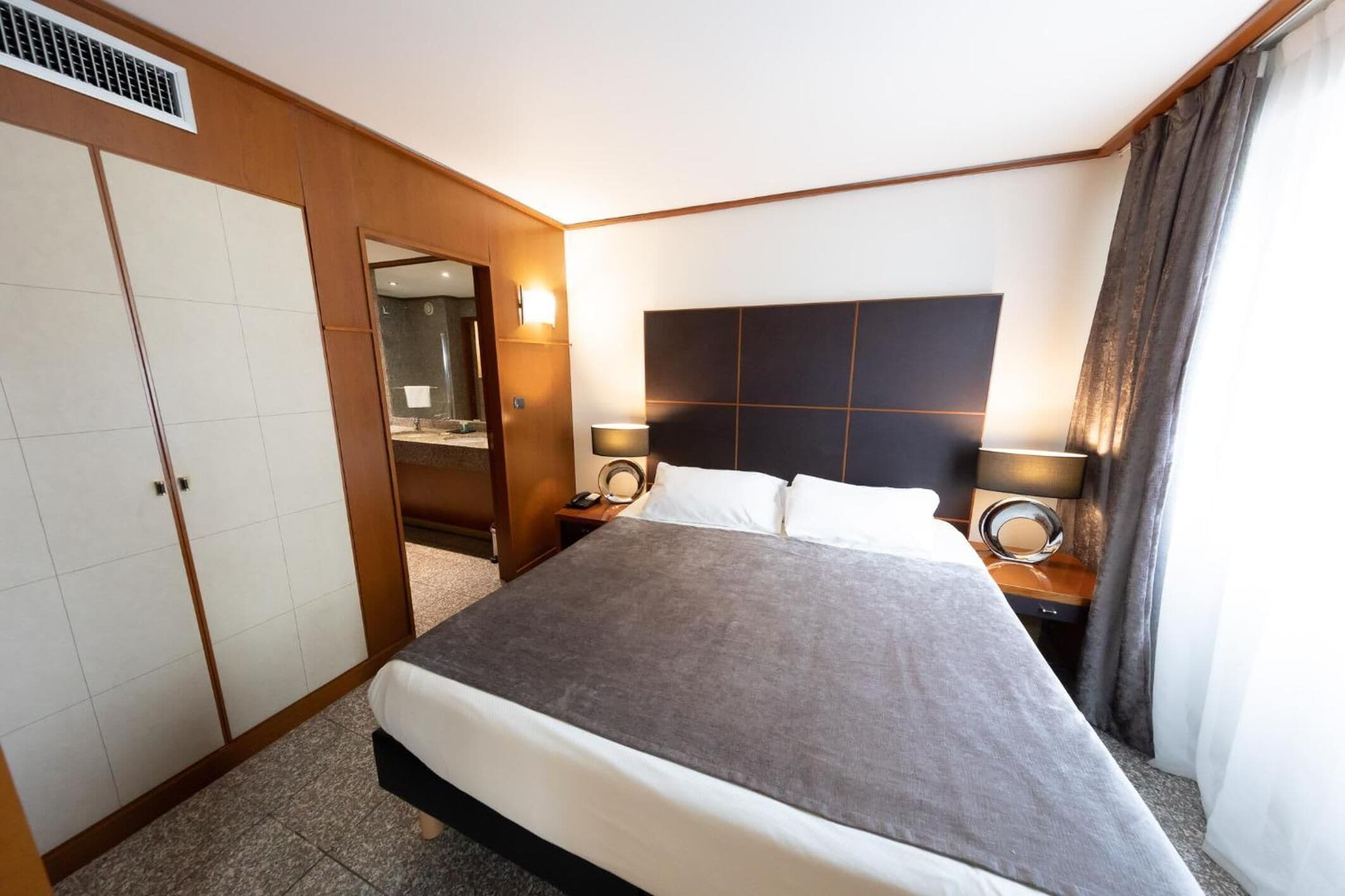 Een hotelkamer met een groot bed, een garderobe, een spiegel en twee bedlampjes.