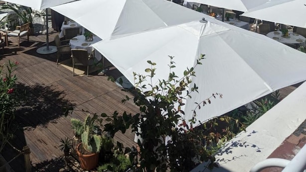 Una terraza con sombrillas blancas y mesas con vista a la playa.