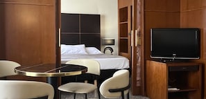 Habitació d'hotel amb un llit, televisió, escriptori i dues cadires.