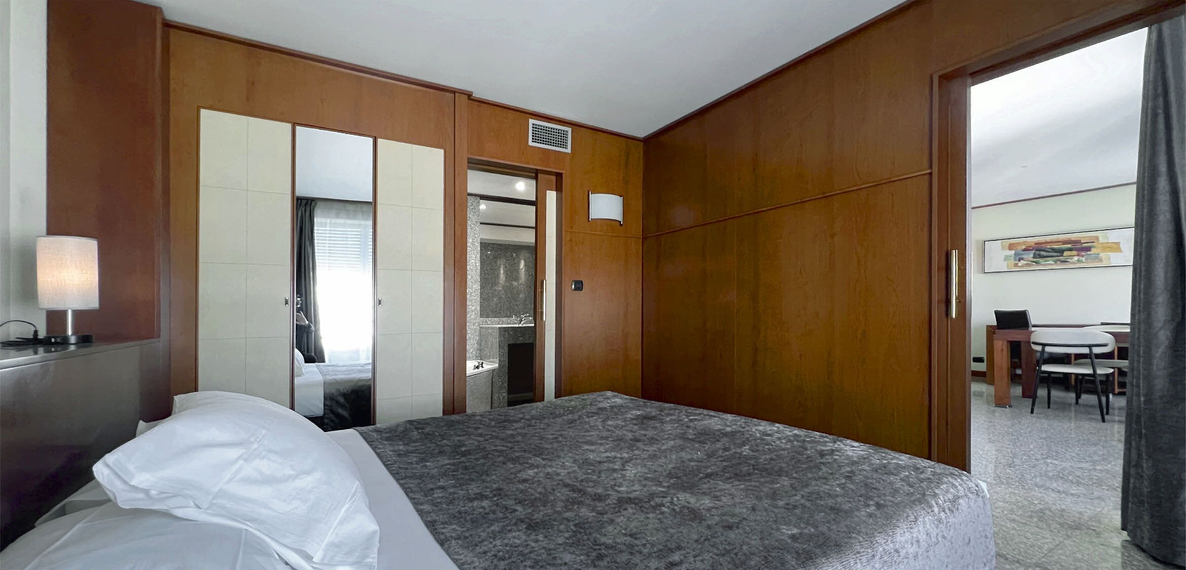 Een hotelkamer met een bed, een bureau, een stoel, een spiegel en een deur naar een badkamer.