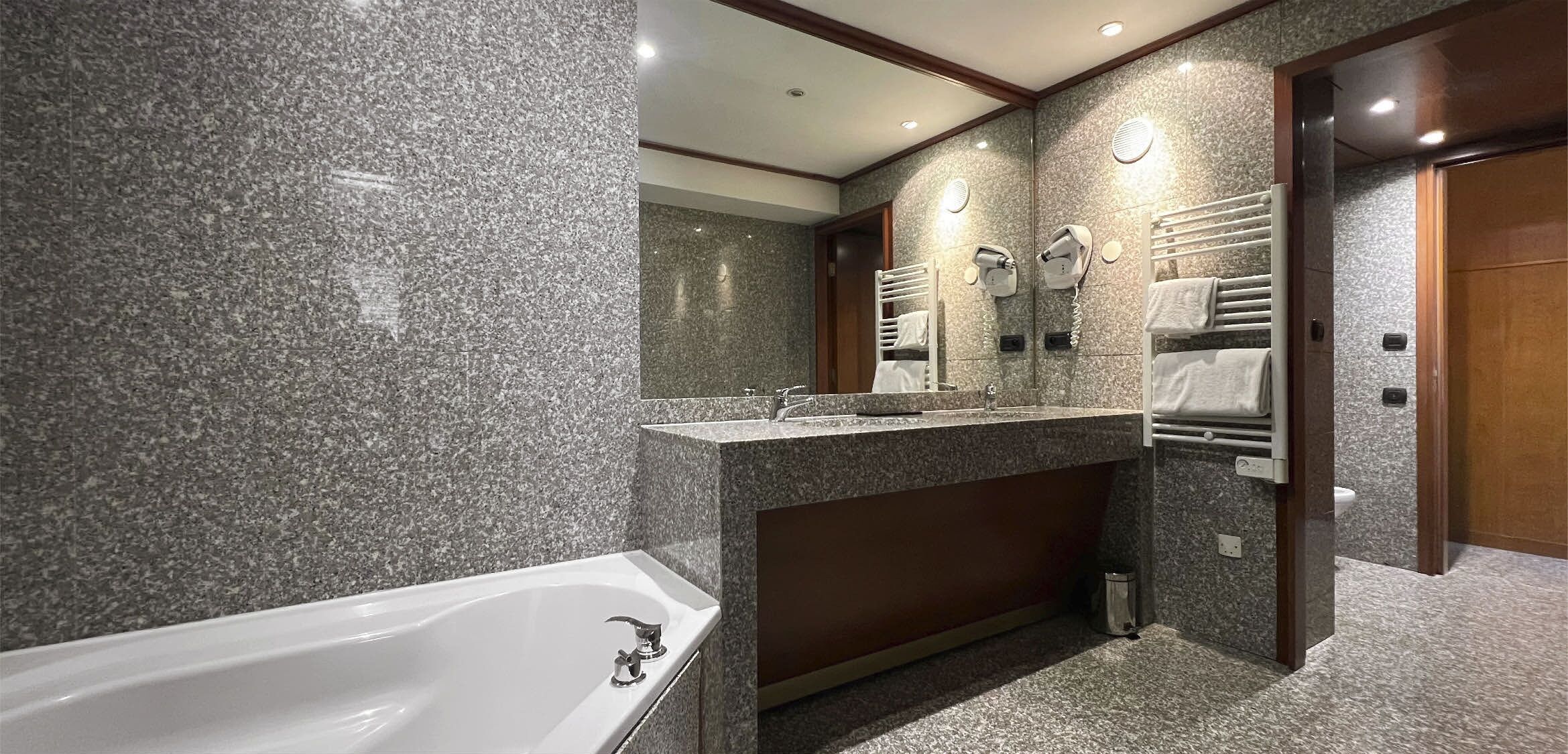 A modern bathroom with a granite countertop, a white bathtub, and a towel rack with towels.