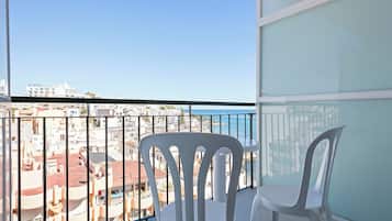 Un balcon avec deux chaises blanches, une balustrade en verre et une vue sur le paysage urbain et la mer.