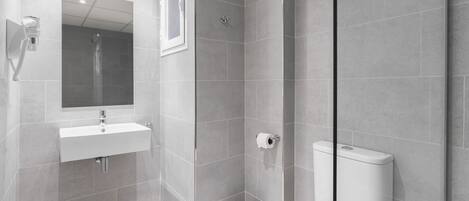 A modern bathroom with a shower, toilet, sink, and a glass partition.