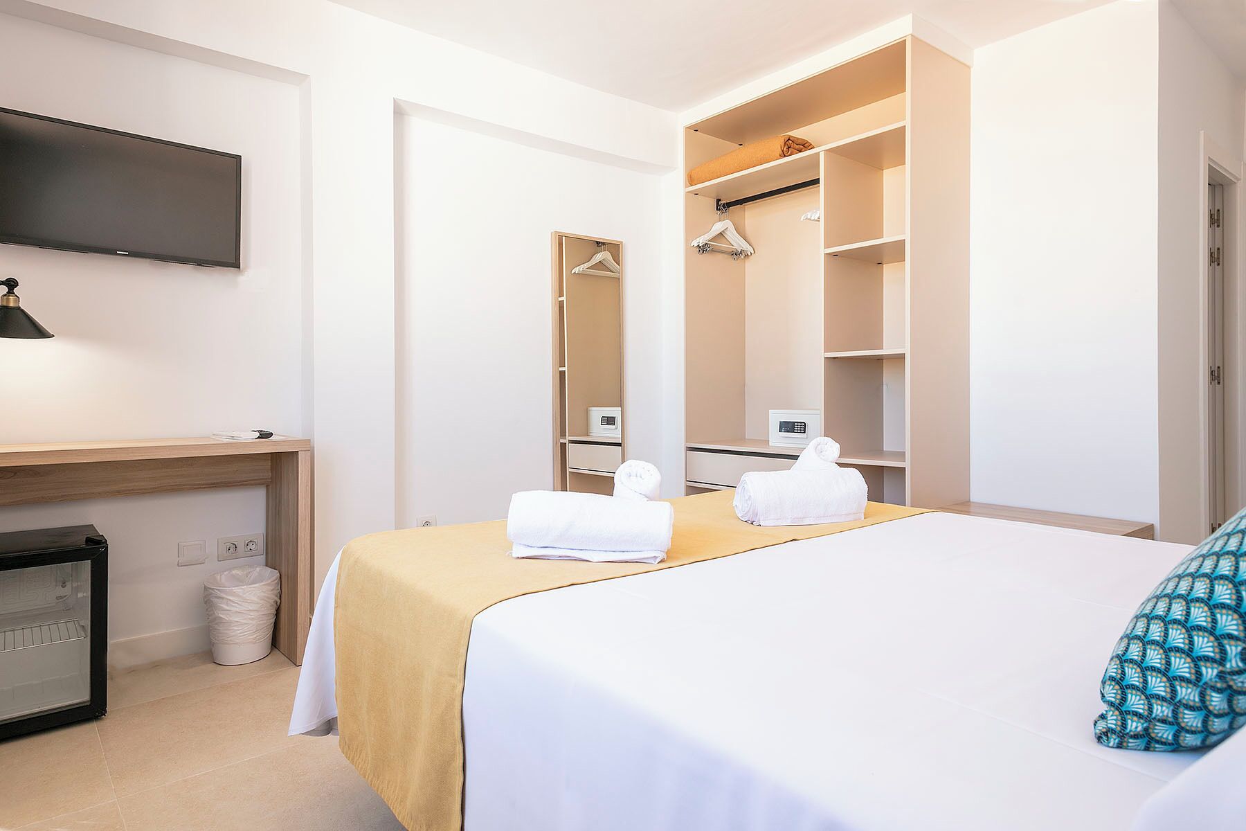 A hotel room with a bed, a desk, a television, a wardrobe, and a trash bin.