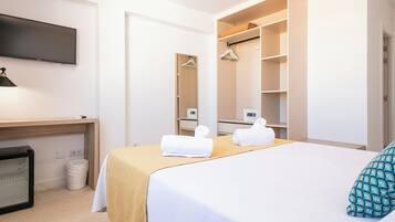 A hotel room with a bed, a desk, a television, a wardrobe, and a trash bin.