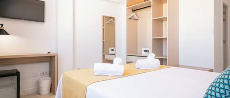 A hotel room with a bed, a desk, a television, a wardrobe, and a trash bin.