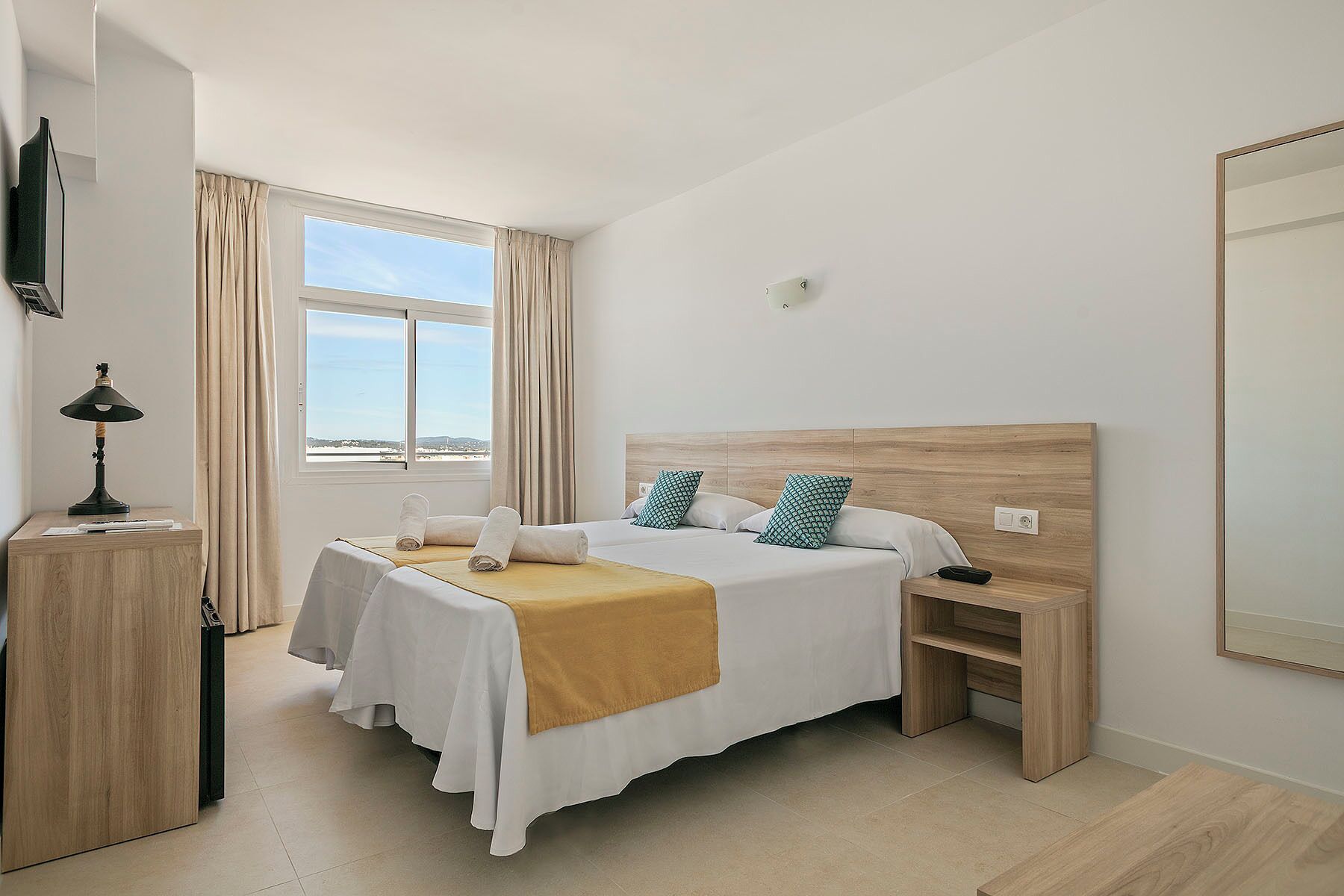 A hotel room with a bed, bedside table, lamp, and a large window.