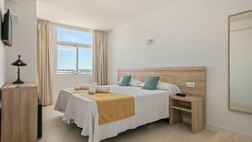 A hotel room with a bed, bedside table, lamp, and a large window.
