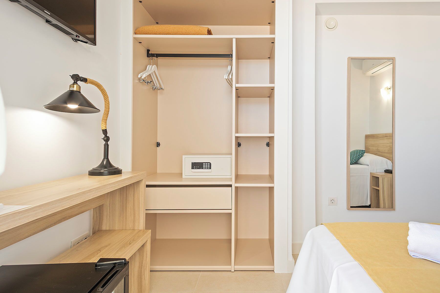 Un dormitorio con cama, mesita de noche, lámpara, armario y espejo.