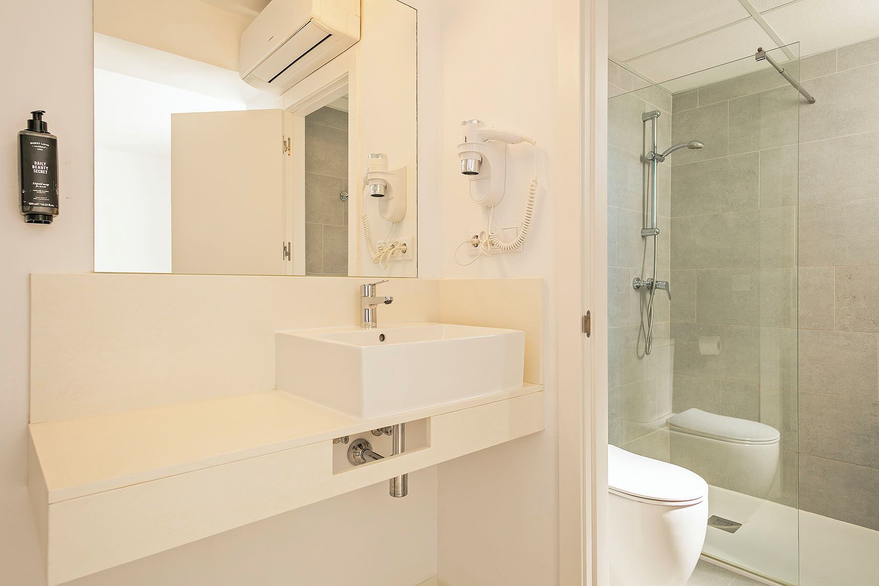 Un baño moderno con lavamanos blanco, espejo y cabina de ducha con mampara de vidrio.