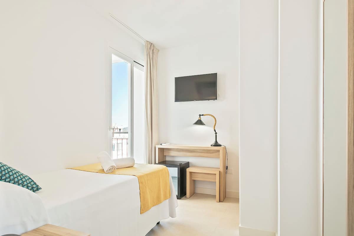 Une chambre d’hôtel avec un lit, un bureau, une chaise, une télévision et une fenêtre avec des rideaux.