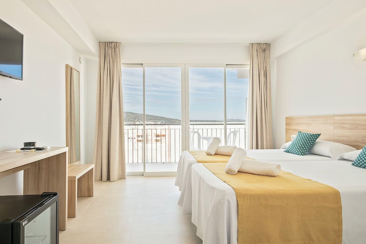 Une chambre d’hôtel avec un lit, un bureau, une télévision et un balcon offrant une vue.