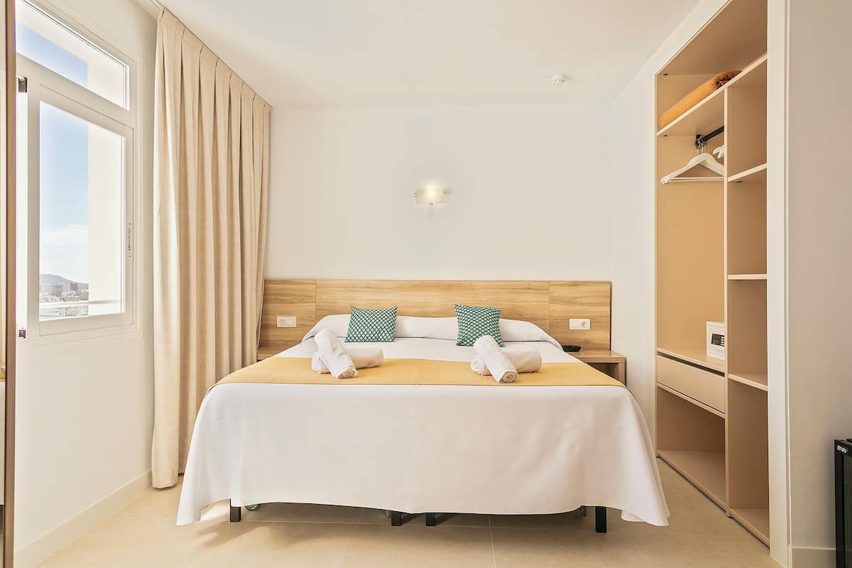 Une chambre d’hôtel avec un lit, une table de chevet, une armoire et une fenêtre avec des rideaux.