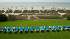 A beach with rows of blue lounge chairs and umbrellas, a sandy path, and a view of the ocean. - Ocean Park Resort by Vacasa (Myrtle Beach)