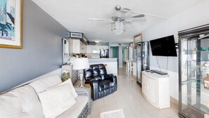 A modern living room with a sofa, a black leather chair, a glass cabinet, and a ceiling fan. - Ocean Park Resort by Vacasa (Myrtle Beach)