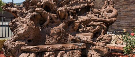 A large, intricate sculpture of intertwined figures and animals, possibly mythological, set against a stone wall.