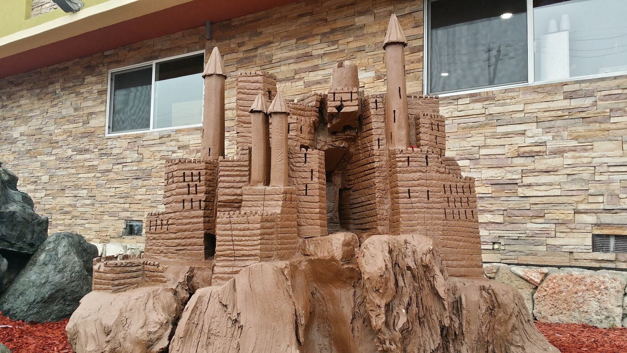 A sandcastle structure with multiple towers and a base, set against a stone wall backdrop.