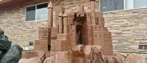 A sandcastle structure with multiple towers and a base, set against a stone wall backdrop.