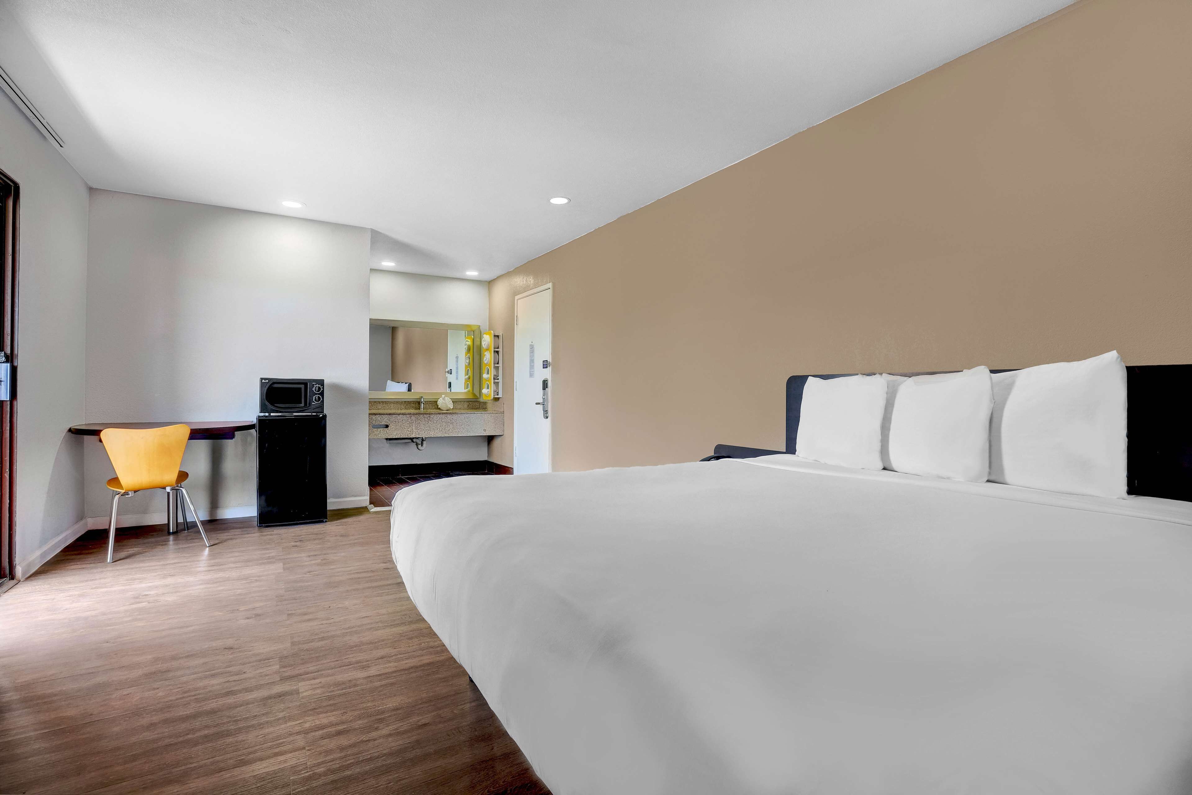 A hotel room with a large bed, a desk, a chair, and a kitchenette area.