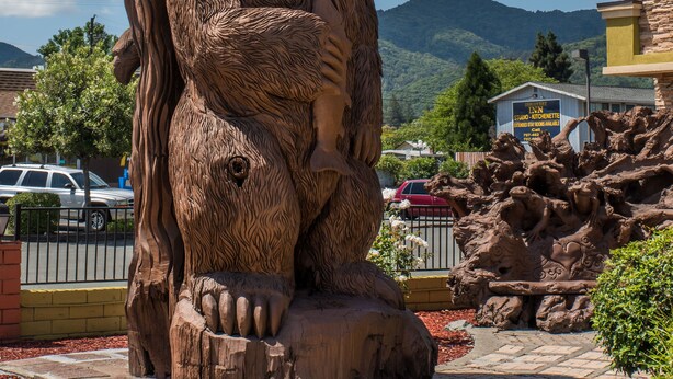 Una gran escultura de oso de madera en un entorno al aire libre con montañas al fondo.