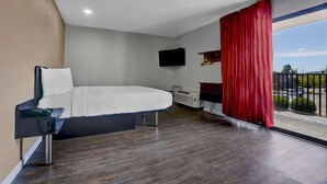 Habitación de hotel moderna con cama, televisor de pantalla plana, escritorio y ventana con cortinas rojas.