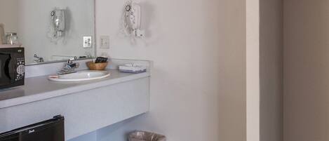 A bathroom with a white sink, a mirror, a hairdryer, and a trash bin.