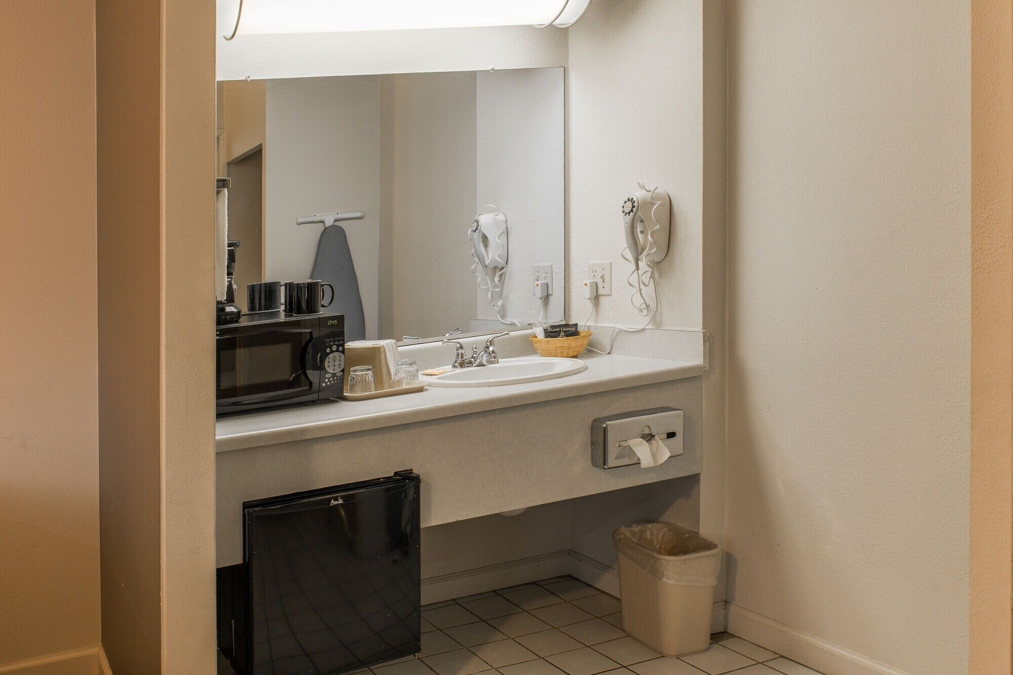 Een kleine badkamer met een wastafel, spiegel en een magnetron.
