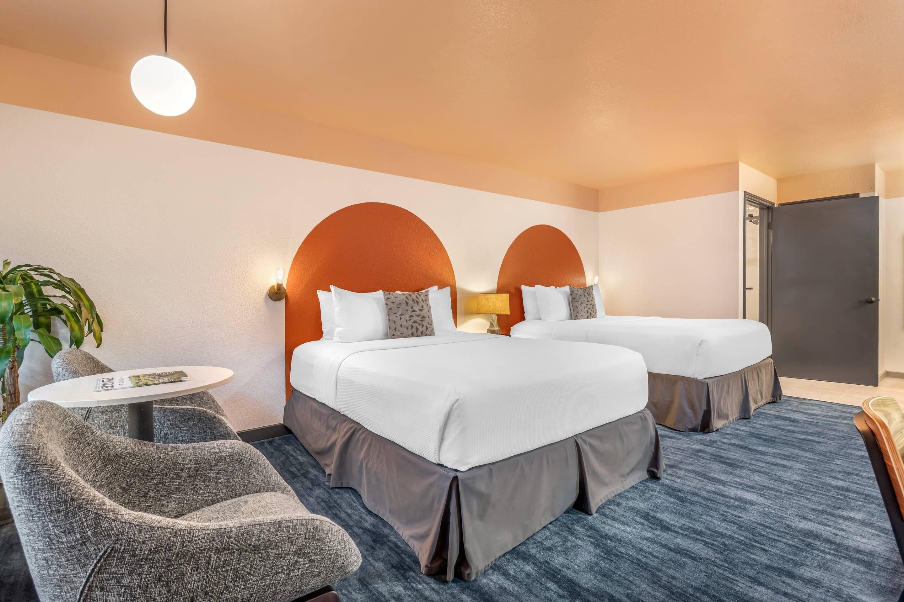 A hotel room with two beds, a small table, a chair, and a potted plant.