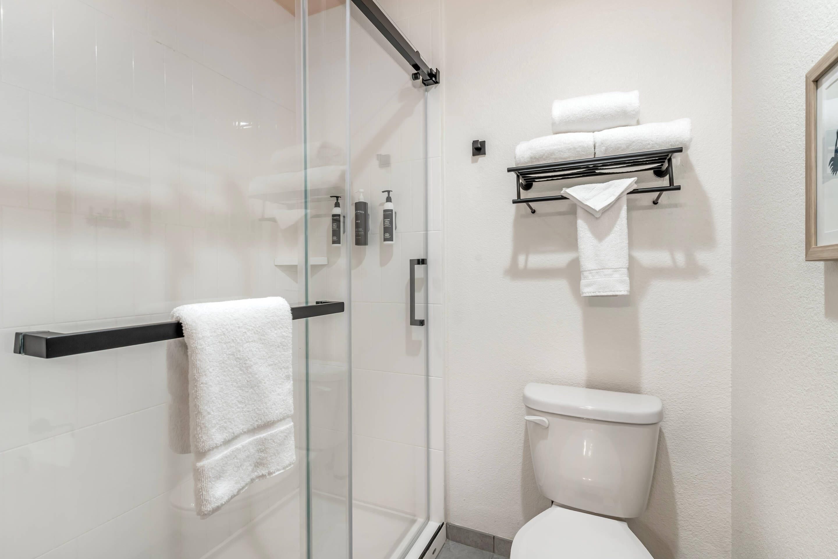 A modern bathroom with a glass shower enclosure, a toilet, and a towel rack with multiple towels.