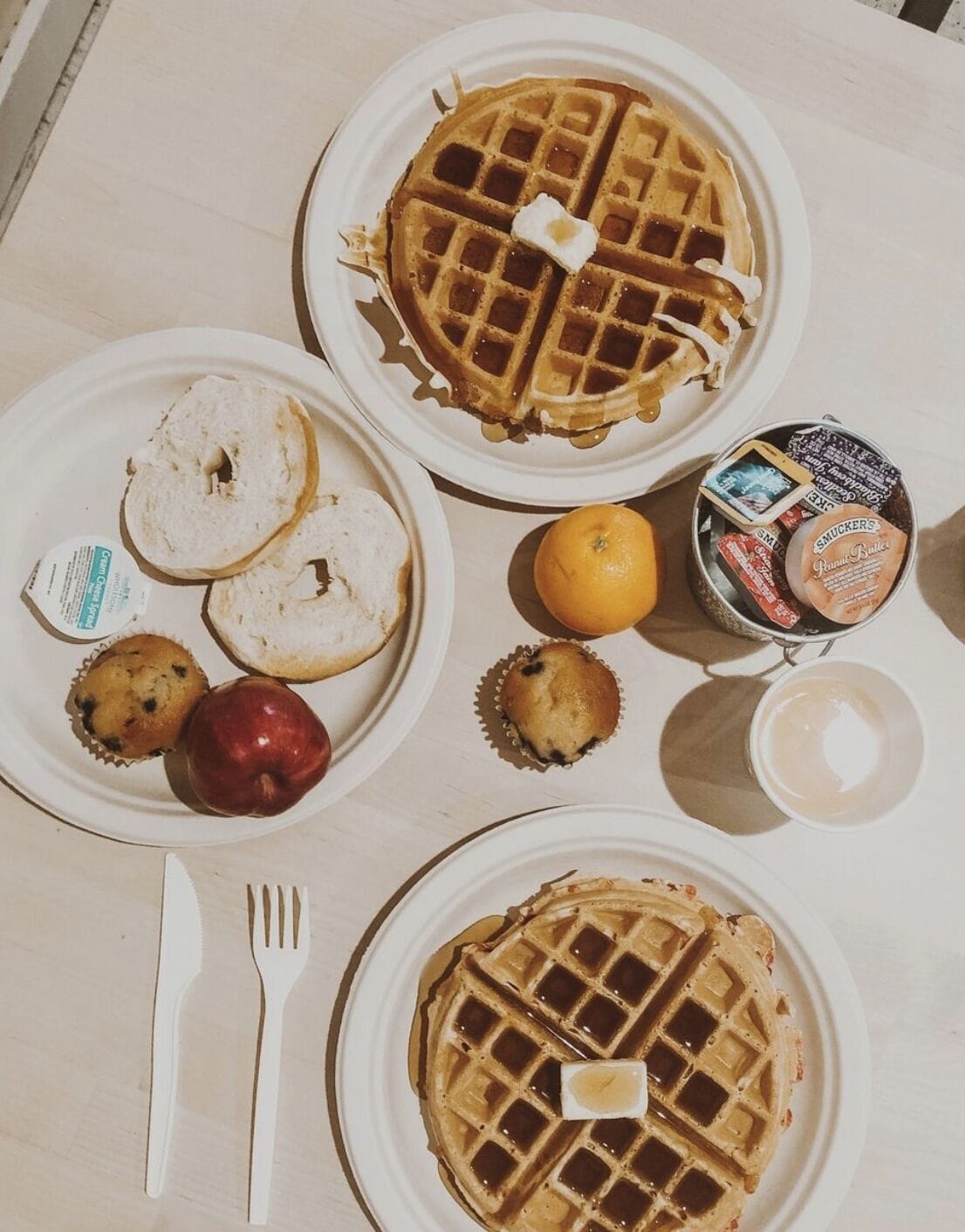 A breakfast setting with waffles, bagels, muffins, and a small orange on a table.