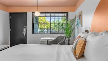 Una habitación de hotel moderna con una cama grande, una mesa redonda, una silla y un ventanal con vistas a árboles.