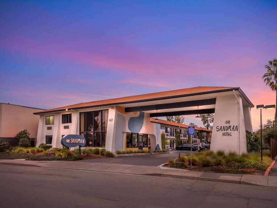 The Sandman Hotel with a modern design, a prominent entrance, and a clear view of the parking area.