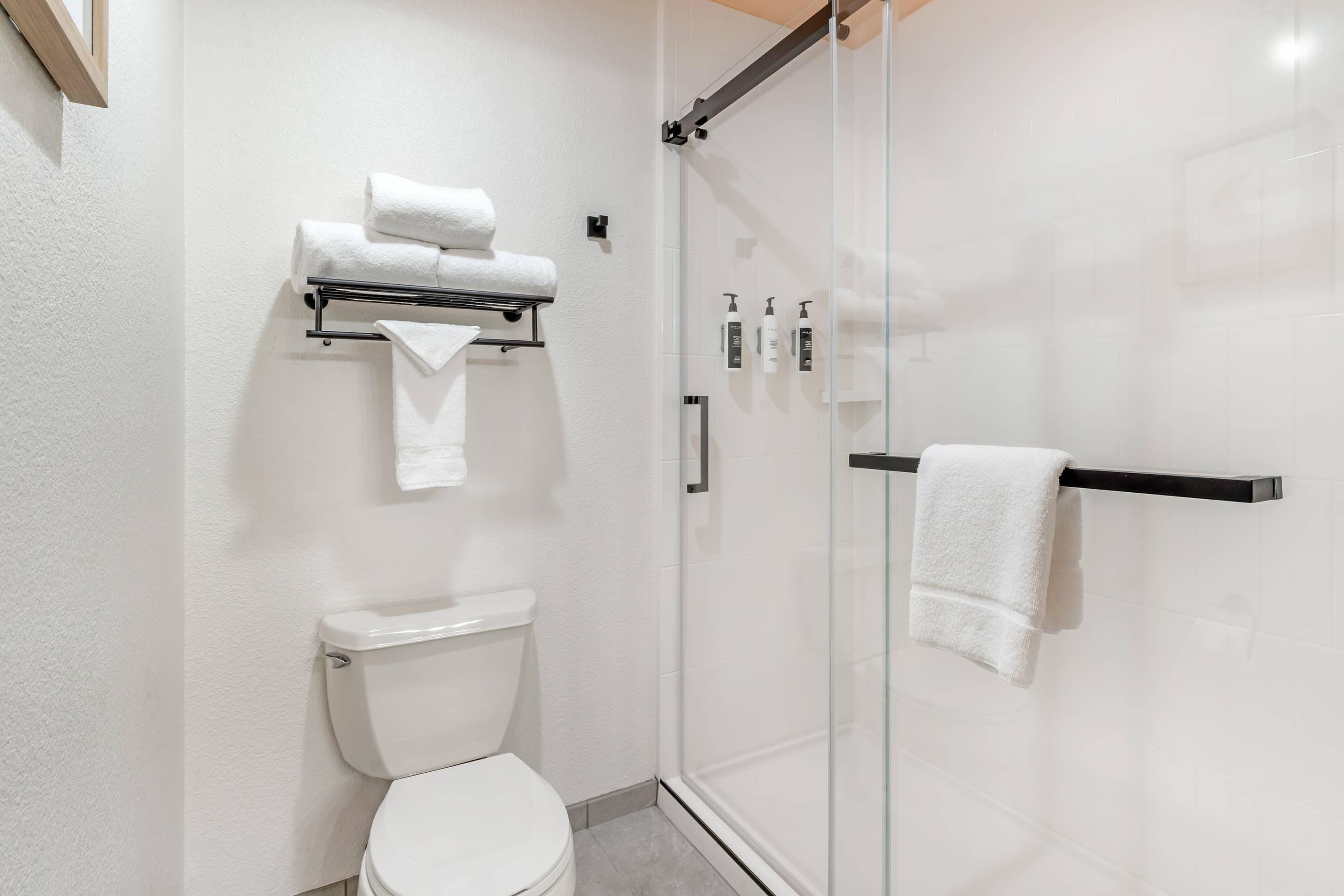 A modern bathroom with a glass-enclosed shower, a white toilet, and a towel rack with neatly folded towels.