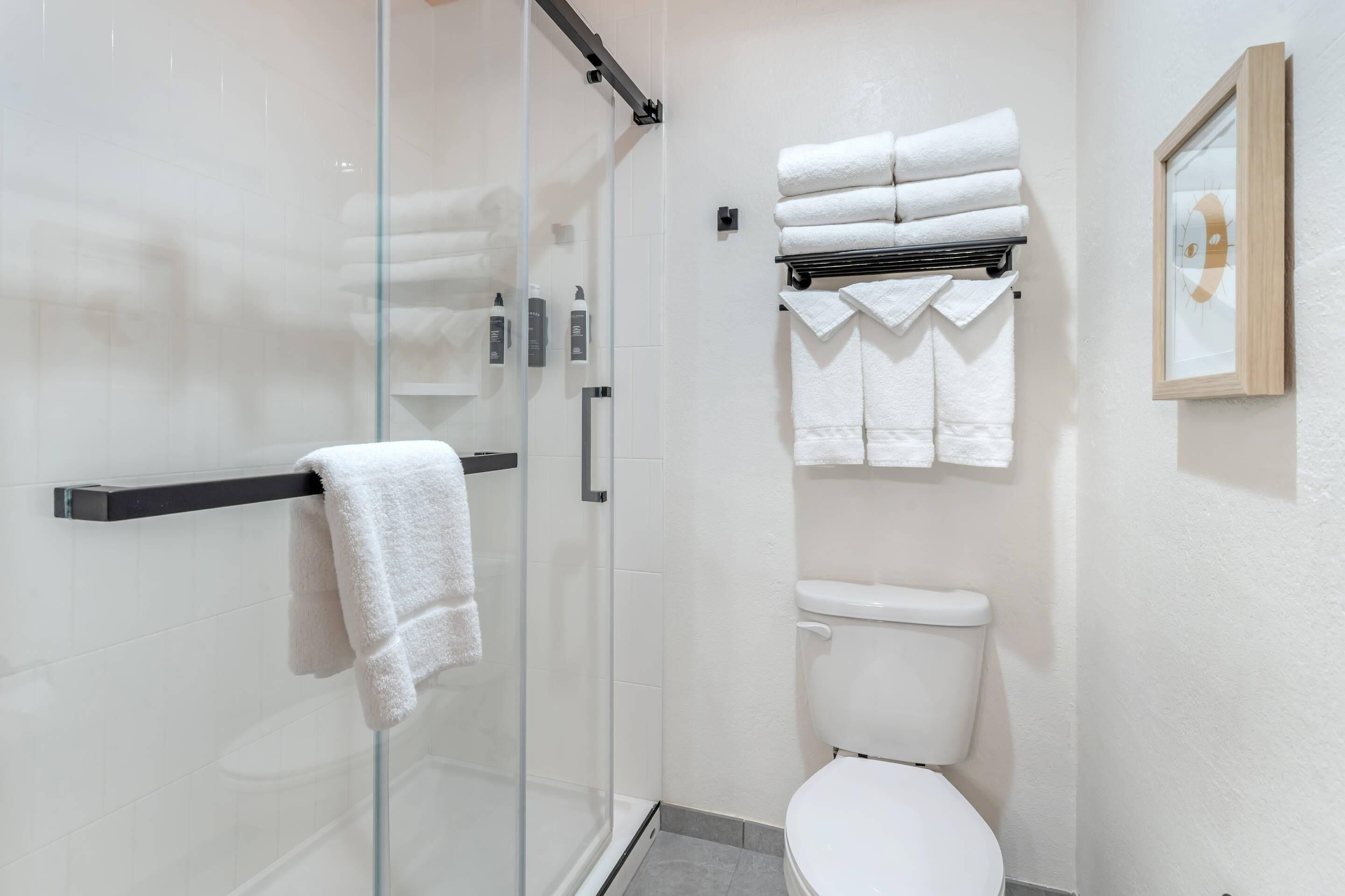 Ein modernes Badezimmer mit Duschkabine aus Glas, Toilette und Handtuchhalter mit ordentlich gefalteten Handtüchern.
