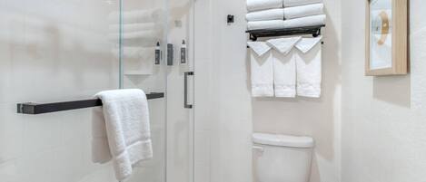 A modern bathroom with a glass shower enclosure, a toilet, and a towel rack with neatly folded towels.