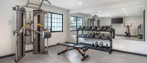 A modern gym with weight machines, benches, dumbbells, and kettlebells.