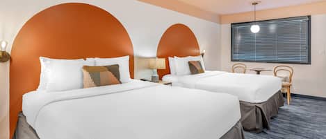 A hotel room with two beds, a small table, and a window with blinds.