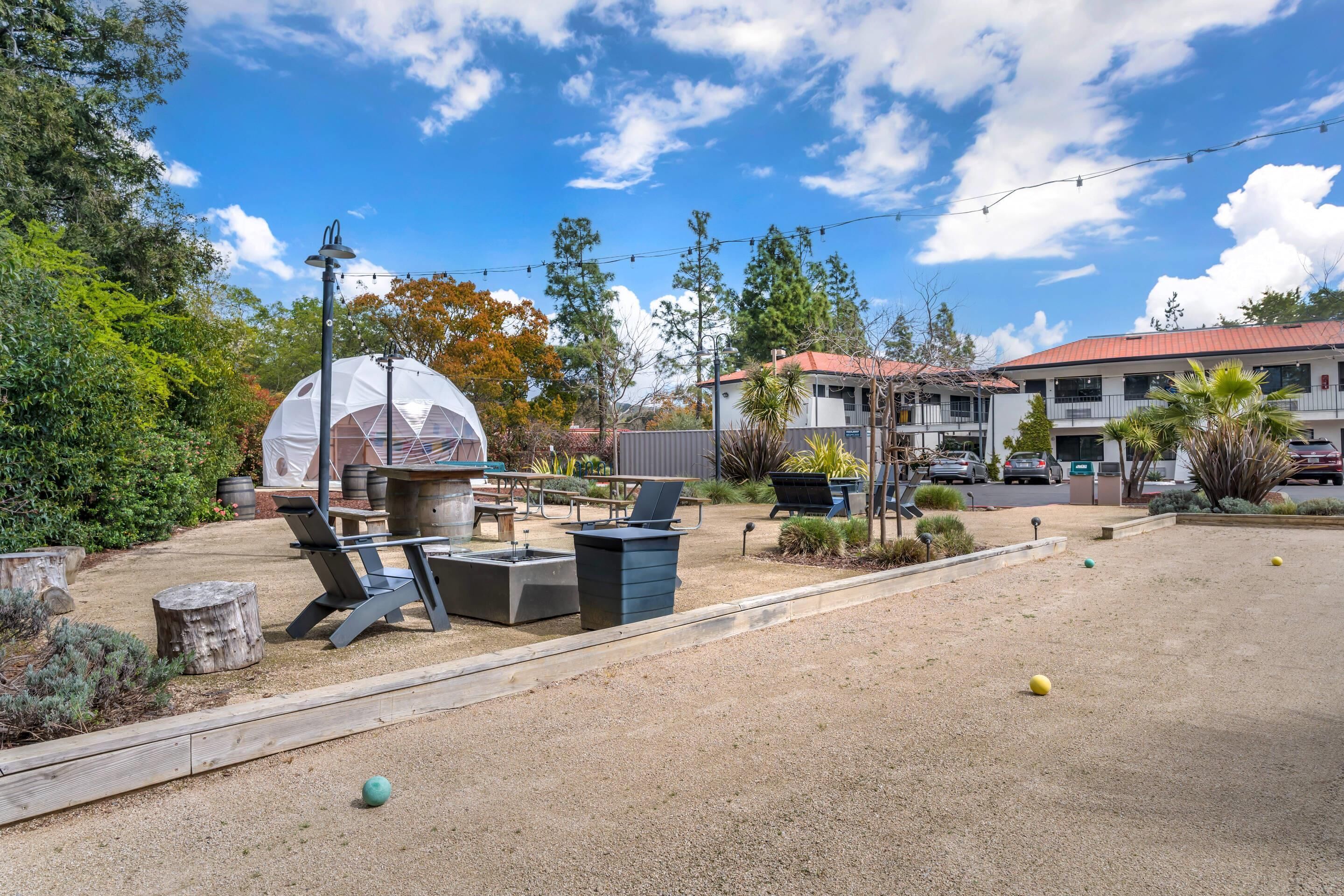 An outdoor seating area with lounge chairs and a fire pit, surrounded by a landscaped garden and a large dome structure.