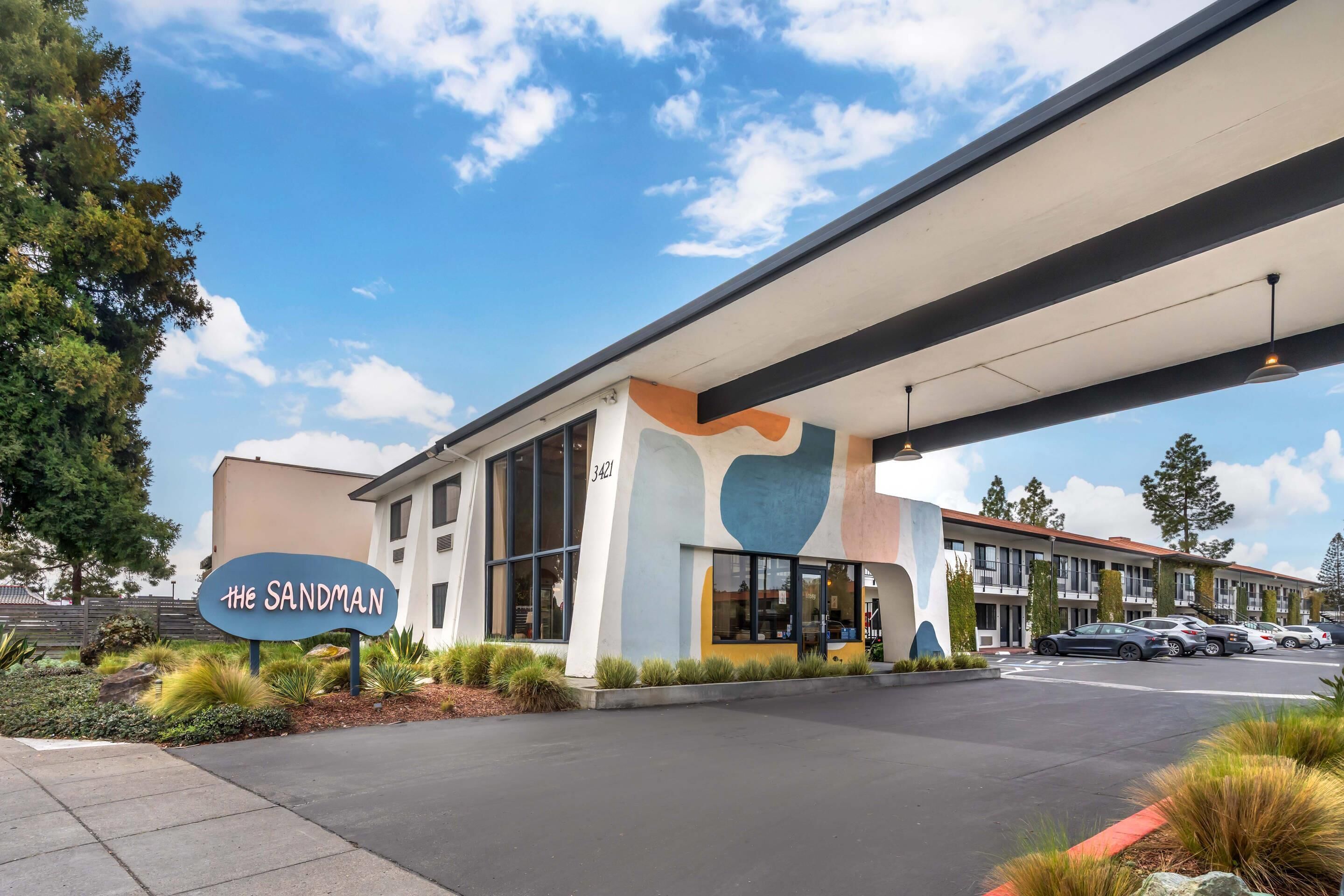 A modern hotel with a distinctive sign, large windows, and a parking area.