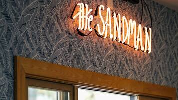 Un bar avec une enseigne au néon sur laquelle on peut lire « The Sandman » et une fenêtre donnant sur une cour arrière.