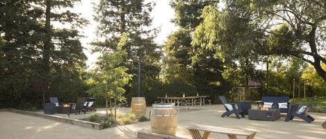 An outdoor seating area with wooden tables and chairs, fire pits, and large barrels.