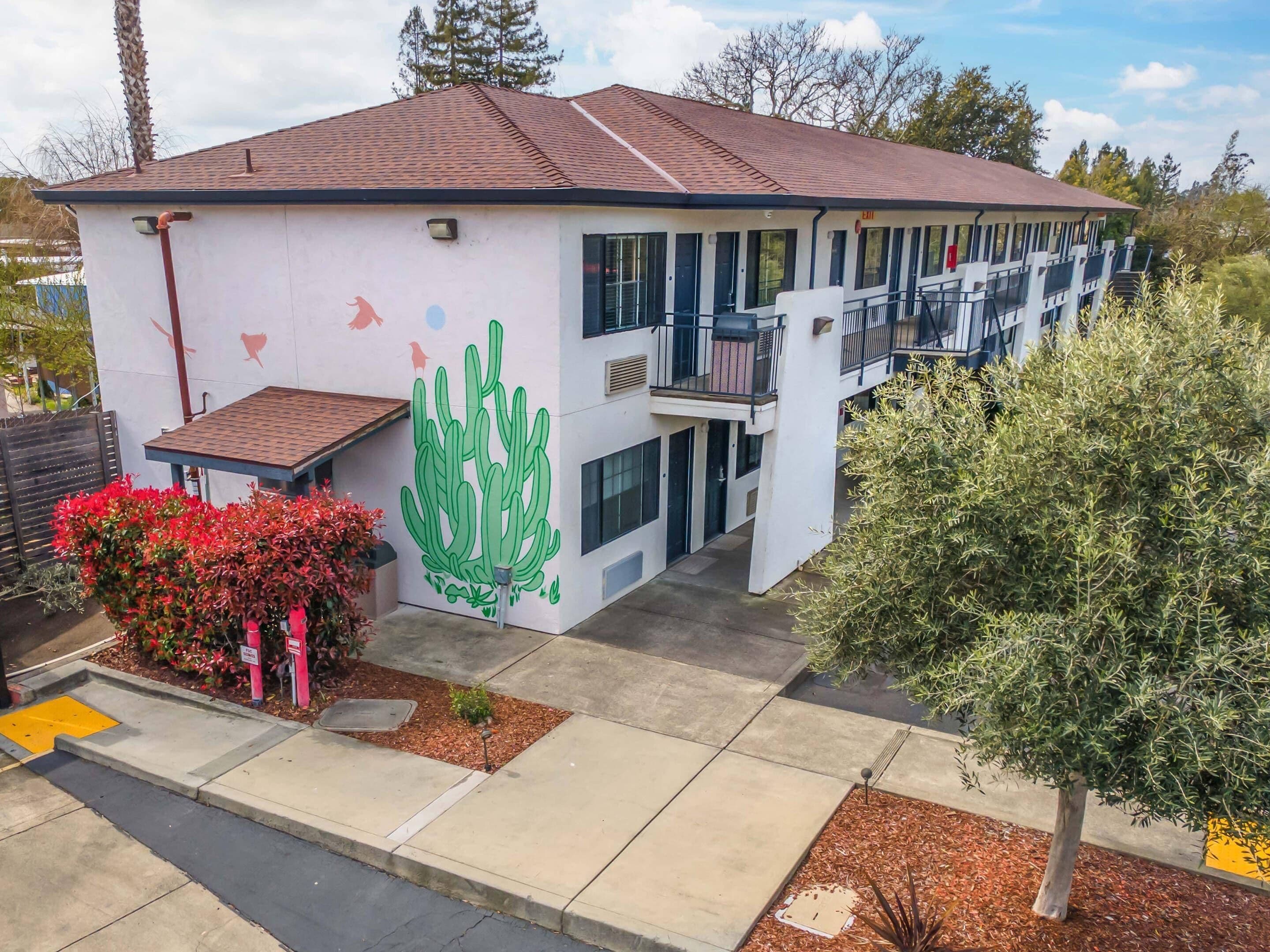 Un bâtiment à deux étages, doté d’un toit plat, d’une grande fresque représentant un cactus sur le mur latéral et d’un balcon à l’étage supérieur.