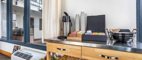 Een moderne keuken met een rvs aanrecht, een koffiezetapparaat, gestapelde bekers en een kom met keukengerei.