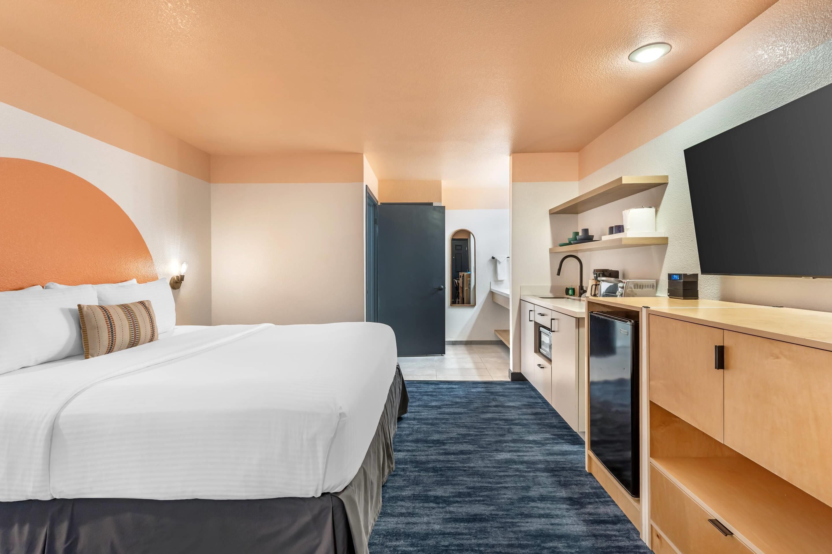 A hotel room with a bed, a desk, a refrigerator, and a bathroom visible through an open door.